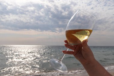 Bir bardak beyaz şarap. Deniz kıyısının arka planında şarap ve güneşli bir yaz plajı. Tatil köyünde şarap tatma ve rahatlama.