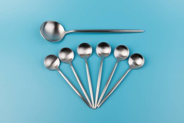 Temiz, boş bir masa kaşığı ve mavi arka planda küçük kaşıklar. Yemek ve mutfak eşyaları konsepti