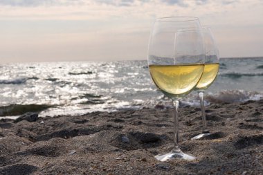 Bir bardak beyaz şarap. Deniz kıyısının arka planında şarap ve güneşli bir yaz plajı. Tatil köyünde şarap tatma ve rahatlama.