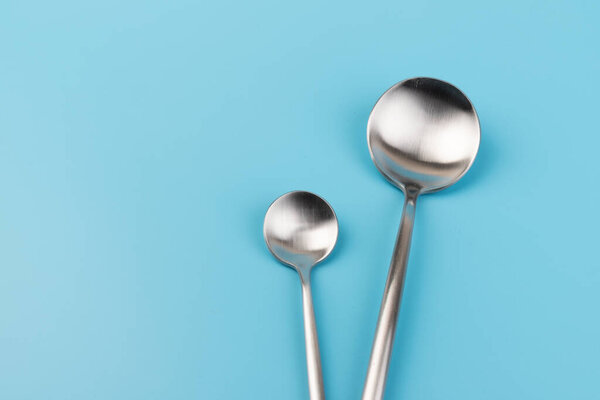 Clean empty  big table spoon and small spoons on blue background, top view. Dining and kitchenware concept