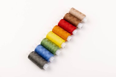 Beyaz arka plandaki makaralara farklı renklerde iplikler dikiyorum. Boş alan, yakın plan.