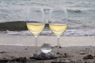 Bir bardak beyaz şarap. Deniz kıyısının arka planında şarap ve güneşli bir yaz plajı. Tatil köyünde şarap tatma ve rahatlama.