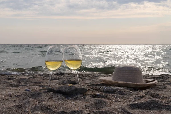 Bir bardak beyaz şarap. Deniz kıyısının arka planında şarap ve güneşli bir yaz plajı. Tatil köyünde şarap tatma ve rahatlama.