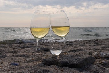 Bir bardak beyaz şarap. Deniz kıyısının arka planında şarap ve güneşli bir yaz plajı. Tatil köyünde şarap tatma ve rahatlama.