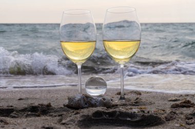 Bir bardak beyaz şarap. Deniz kıyısının arka planında şarap ve güneşli bir yaz plajı. Tatil köyünde şarap tatma ve rahatlama.