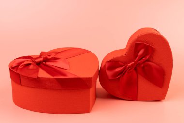 Kırmızı kalp şeklinde hediye paketi ve pembe arka planda kırmızı kurdele. Sevgililer Günün kutlu olsun. Yıldönümü. 
