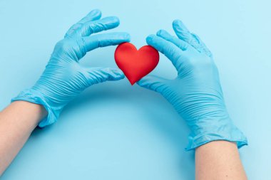 Kadın doktor el ele tutuşup kırmızı oyuncak kalbi kapatıyor. Kardiyoloji kavramı.