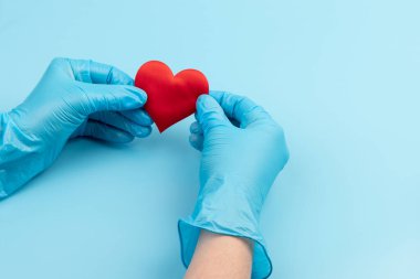Kadın doktor el ele tutuşup kırmızı oyuncak kalbi kapatıyor. Kardiyoloji kavramı.