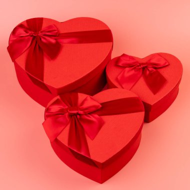Kırmızı kalp şeklinde hediye paketi ve pembe arka planda kırmızı kurdele. Sevgililer Günün kutlu olsun. Yıldönümü. 
