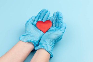 Kadın doktor el ele tutuşup kırmızı oyuncak kalbi kapatıyor. Kardiyoloji kavramı.