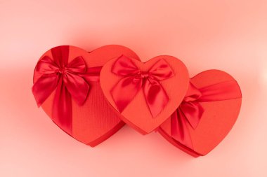 Kırmızı kalp şeklinde hediye paketi ve pembe arka planda kırmızı kurdele. Sevgililer Günün kutlu olsun. Yıldönümü. 