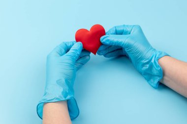 Kadın doktor el ele tutuşup kırmızı oyuncak kalbi kapatıyor. Kardiyoloji kavramı.