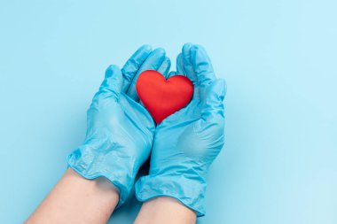 Kadın doktor el ele tutuşup kırmızı oyuncak kalbi kapatıyor. Kardiyoloji kavramı.