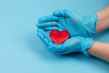 Kadın doktor el ele tutuşup kırmızı oyuncak kalbi kapatıyor. Kardiyoloji kavramı.