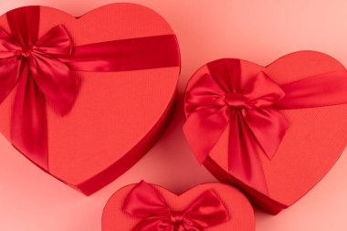 Kırmızı kalp şeklinde hediye paketi ve pembe arka planda kırmızı kurdele. Sevgililer Günün kutlu olsun. Yıldönümü. 