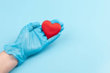 Kadın doktor el ele tutuşup kırmızı oyuncak kalbi kapatıyor. Kardiyoloji kavramı.