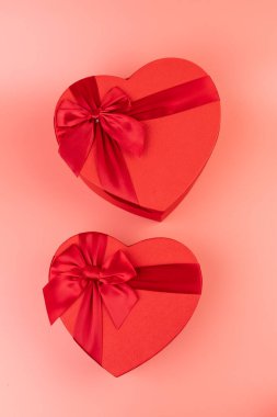 Kırmızı kalp şeklinde hediye paketi ve pembe arka planda kırmızı kurdele. Sevgililer Günün kutlu olsun. Yıldönümü. 
