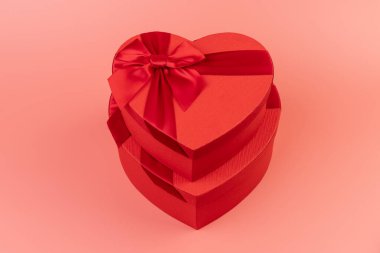 Kırmızı kalp şeklinde hediye paketi ve pembe arka planda kırmızı kurdele. Sevgililer Günün kutlu olsun. Yıldönümü. 