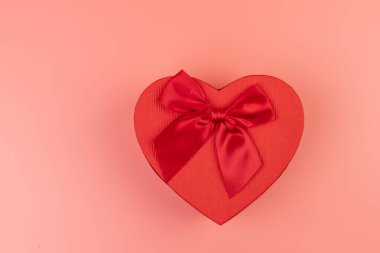 Kırmızı kalp şeklinde hediye paketi ve pembe arka planda kırmızı kurdele. Sevgililer Günün kutlu olsun. Yıldönümü. 