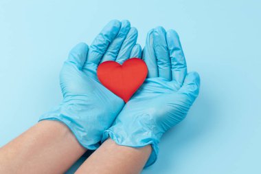 Kadın doktor el ele tutuşup kırmızı oyuncak kalbi kapatıyor. Kardiyoloji kavramı.