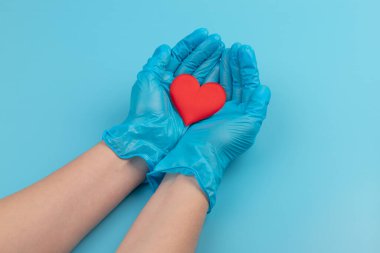 Kadın doktor el ele tutuşup kırmızı oyuncak kalbi kapatıyor. Kardiyoloji kavramı.