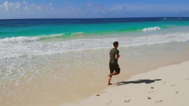 Formda bir adam okyanus kıyısında ağır çekimde sörf yapar.