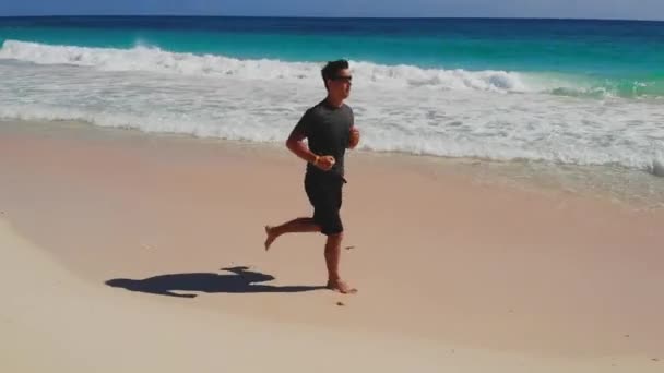 Homem atlético correr ao longo do oceano surf pela praia arenosa — Vídeo de Stock