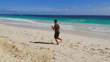 Genç adam sahilde yalın ayak koşuyor, ağır çekimde.