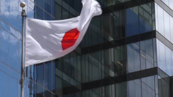 Japońska flaga narodowa macha wiatrem przeciwko nowoczesnemu budynkowi, zwolniony ruch — Wideo stockowe