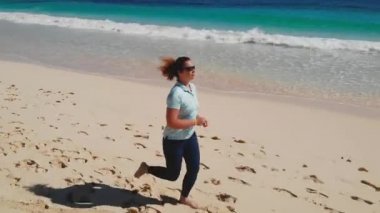 Tombul ve mutlu orta yaşlı bir kadın plajda koşuyor. 30 'lu ya da 40' lı yaşlarda, kahverengi saçlı, çekici ve olgun bir kadın. Koşu yapıyor.