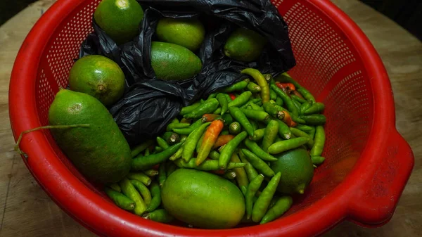 Tahtadaki kırmızı sepetin içinde yeşil kırmızı biberli bir paket limon. Yakın çekim yiyecek ve meyveler.. 