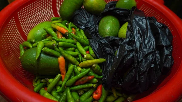 Tahtadaki kırmızı sepetin içinde yeşil kırmızı biberli bir paket limon. Yakın çekim yiyecek ve meyveler.. 