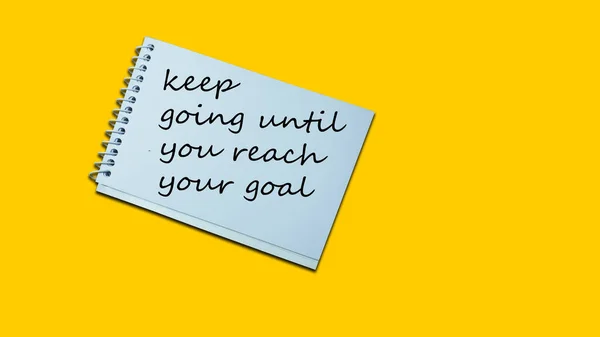keep going until you reach your goal Hand writing note on a notebook. lifestyle, advice, support motivational positive words are written on a wooden background. Business, signs, symbols, concepts. Copy space.