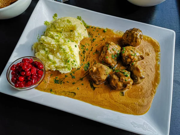 Swedish typical dish consisting of meatballs with sauce, mashed potatoes and ribes. Tasty recipe with Swedish meat balls floating on thick gravy with smashed potatoes covered with sprinkling parsley