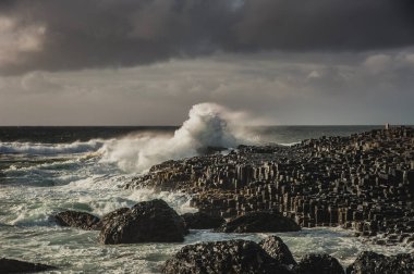 Kasvetli bir günde, okyanus dalgaları altıgen kayalara çarpıyor. Altıgen, uçuruma çarpan deniz dalgalı taşlar güçlü bir etki ya da büyük bir etki konsepti taşır. Antrim İlçesi, Kuzey İrlanda, Birleşik Krallık