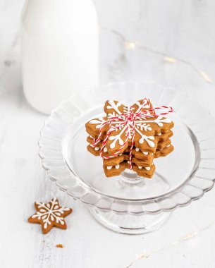 Bir yığın kar tanesi zencefilli kurabiye bir ip ve parlak beyaz arka planda bir şişe sütle bağlanmış. Noel arifesinde Noel Baba için geleneksel hediye..