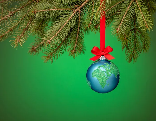 Globe christmas ornament hanging from a tree branch on green. Peace on Earth, eco friendly or winter travel concept.