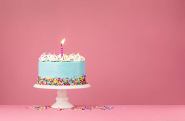 Renkli serpiştirilmiş mavi doğum günü pastası ve pembe arka planda yanan doğum günü mumu..