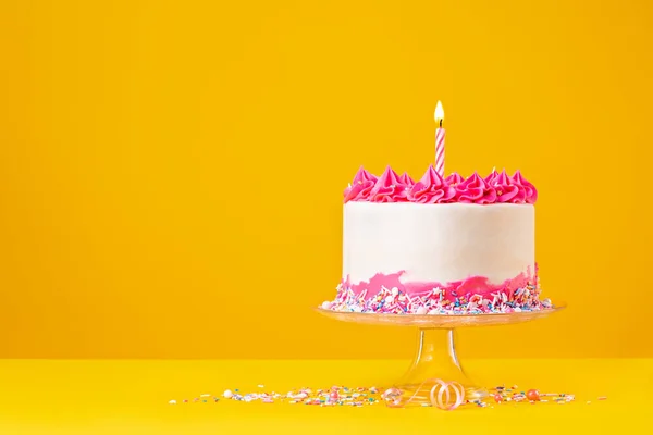 ピンクのバタークリームアイシング カラフルなスプリンクル 明るい飽和黄色の背景にライト付きの誕生日キャンドル付きの誕生日ケーキ — ストック写真