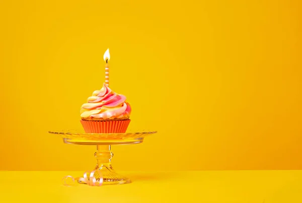 鮮やかで飽和した黄色の背景に縞模様のキャンドルとピンクとオレンジのアイス誕生日カップケーキ 楽しさと陽気な誕生日の御馳走 — ストック写真