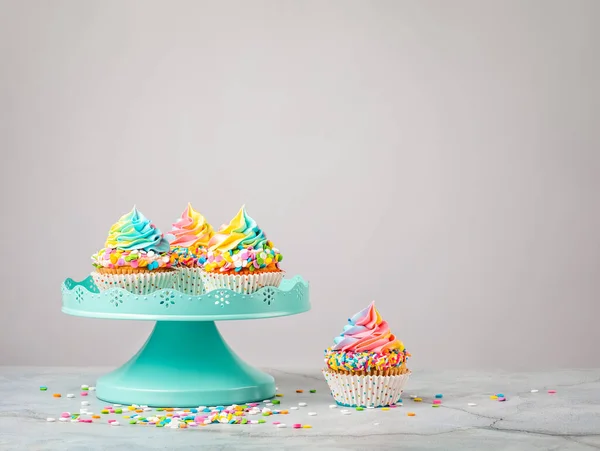 Cupcake Compleanno Arcobaleno Con Spruzzi Colorati Uno Stand Torta Blu — Foto Stock