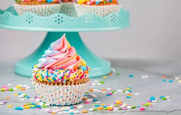 Tęczowy Wir Babeczka Urodzinowa Kolorowymi Posypkami Przed Niebieskim Stojakiem Ciasto — Zdjęcie stockowe