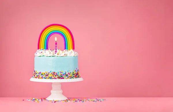 Gâteau d'anniversaire bleu avec dessus arc-en-ciel sur rose — Photo