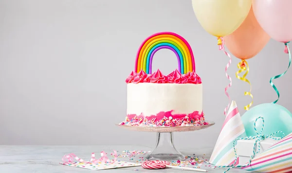Torta di compleanno rosa con decorazione arcobaleno e palloncini ad una festa Foto Stock