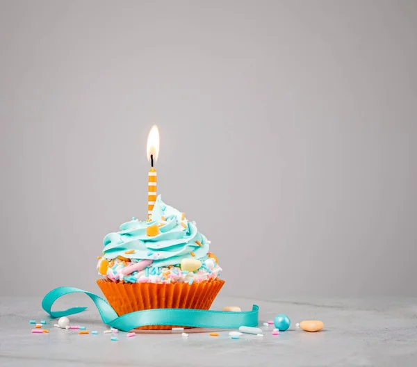 Blue Birthday Cupcake with orange Candle over grey — Stock Photo, Image