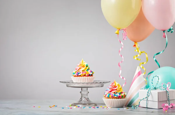 Cupcake di compleanno arcobaleno a una festa con palloncini colorati Foto Stock Royalty Free