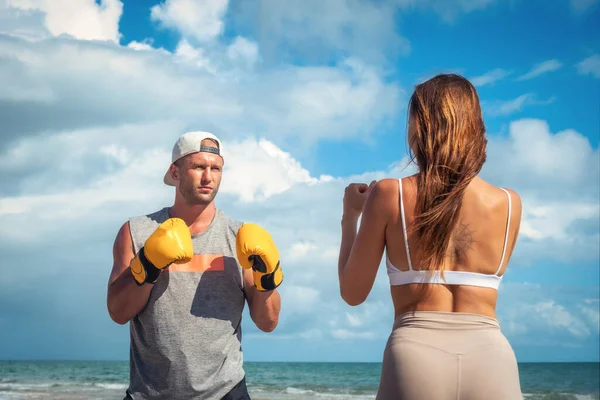 Sport man and woman boxing on beach at sunset