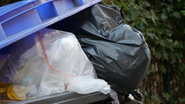 Niebieski kosz na śmieci pełen paczek ze śmieciami na ulicy. Problem zanieczyszczenia środowiska — Wideo stockowe