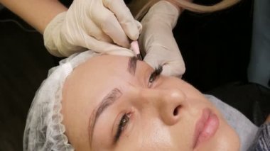 Usta özel kalemle kaşların yeni bir şeklini çizer. Kaş şekli düzeltmesi. Mikro patinaj, kalıcı makyaj, dövme