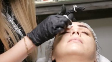 Mikro patinaj için özel bir kalem ve iğne yardımıyla kozmetolojist genç bir kadının kaşlarının şeklini geliştirir. Kaş mikropateni, kalıcı makyaj, dövme.